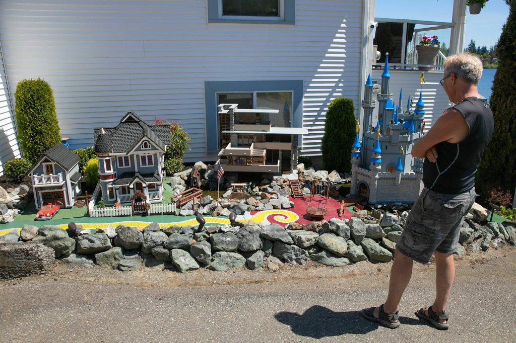 Gary Fontes stands in front of three of his mini homes on Friday, May 12, 2023, at his home near Silver Lake in Everett, Washington. From left are a Victorian home based off a haunted house, Frank Lloyd Wrights Fallingwater and a Disney-style castle. (Ryan Berry / The Herald)