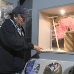 Lewis points to a display case featuring cxelusa bulbs, a hand-woven basket, and a traditional puca made of wood and a piece of antler at the Colville Tribal Museum in Grand Coulee. (Dominick Bonny / Crosscut)