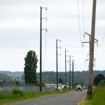 A PUD vehicle drives along Lovers Road under newly-erected power poles that will eventually connect Stanwood and Camano Island on Tuesday, May 30, 2023, in Stanwood, Washington. (Ryan Berry / The Herald)