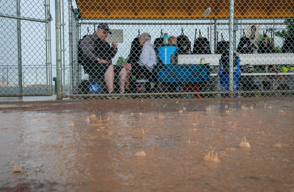 Rain pounds the field while Jackson coaches and volunteers huddle with equipment in the first base dugout at Columbia Playfield on Saturday, May 27, 2023, in Richland. (TJ Mullinax / For The Herald)
