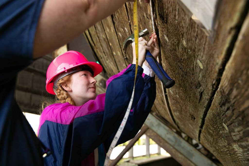 Graduate student Alyssa Carpenter, center, tacks a tape measure to the Equator with the help of undergrad Kimberly Price as the two map out a multitude of fastenings used to hold together the ship on Wednesday, June 7, 2023, during a two-week survey of the vessel at its resting place in Everett, Washington. (Ryan Berry / The Herald)