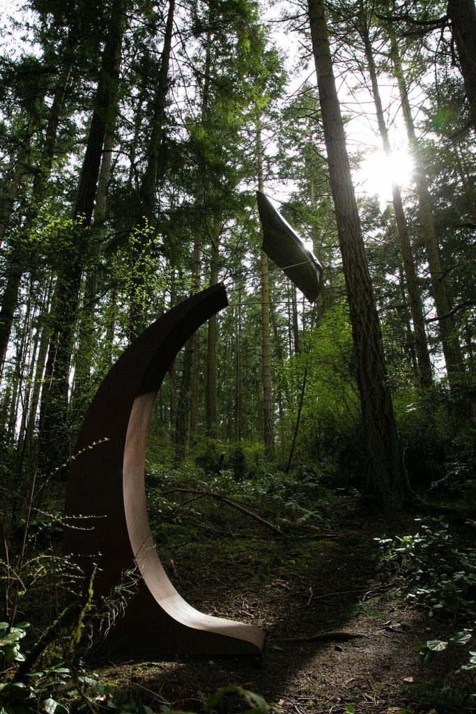 The sun cuts through the trees and reflects off a sculpture at Price Sculpture Forest on Wednesday, April 5, 2023, in Coupeville, Washington. (Ryan Berry / The Herald)
