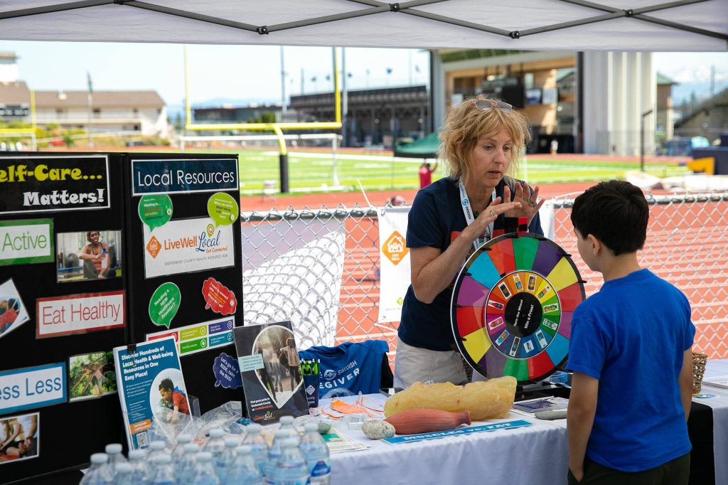 Jessica Burt, director of the Providence Institute for a Healthier Community, speaks with a child about choosing healthy drinks and making good health decisions during the Robert C. Polk Heart Healthy Education Event on Saturday, June 3, 2023, at Memorial Stadium in Everett, Washington. (Ryan Berry / The Herald)