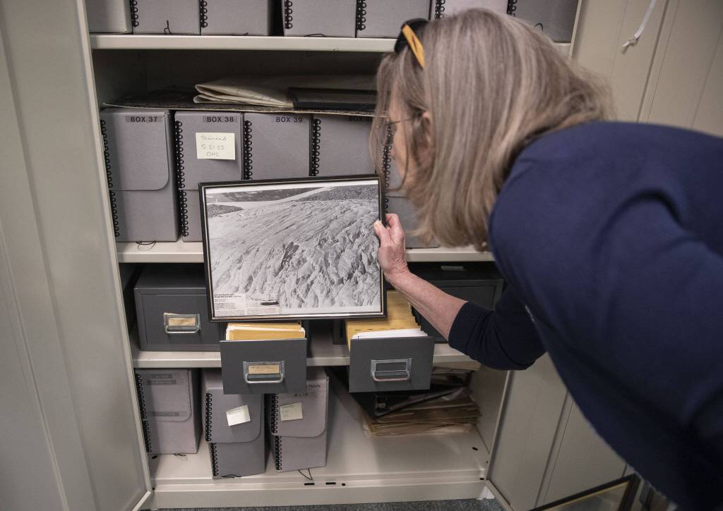 Erika Morris holds up a framed photograph while pulling out documents at the Darrington Ranger Station on Tuesday, June 6, 2023 in Darrington, Washington. (Olivia Vanni / The Herald)