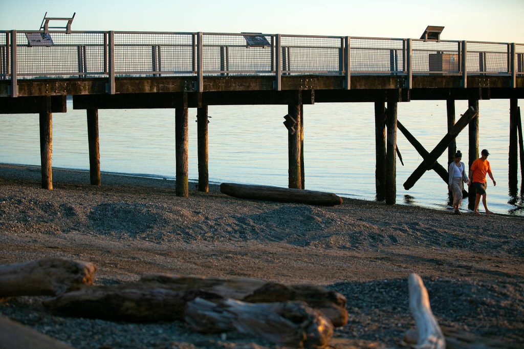 A couple walks along the beach and over the gravelly, muddy boat launch, in the foreground, at Kayak Point on Monday, June 12, 2023, in Stanwood, Washington. (Ryan Berry / The Herald)