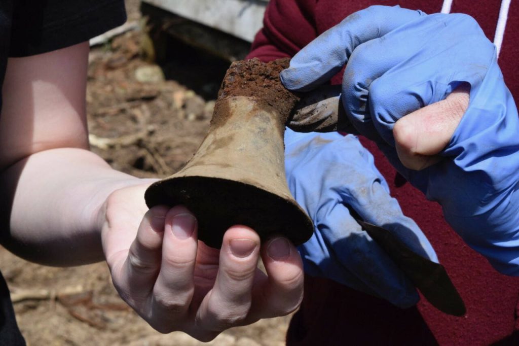 Woodhaven School freshman Alicia Jenkins shows off the metal bell she found to property owner Marian Myszkowski. (Photo by Patricia Guthrie)