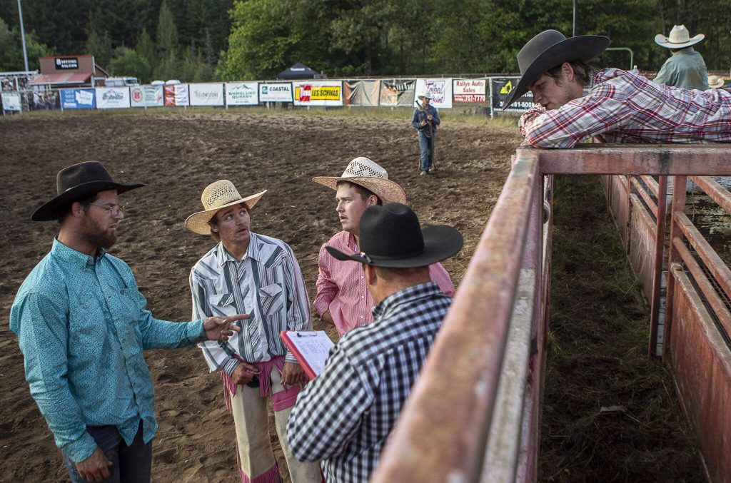 Left to right, Ryan Anderson, 36, Kadyn Wilson, 20, Jake Iverson, 23, and Trey Butler, 19, listen to a judge who checks his clipboard during the Timberbowl Rodeo in Darrington, Washington on Saturday, June 24, 2023. (Annie Barker / The Herald)