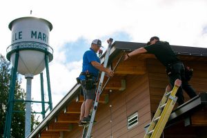 Tyler Giles, owner/operator of Giles Electric, left, gets a helping hand from lead field tech Quintin Viers as they work to install the last bit of LED trim lights along the roof of a new bathroom on the Marysville Civic Center campus on Friday, June 30, 2023, in Marysville, Washington. The lights, which can be programmed to different colors, have also been installed on the main Civic Center building. (Ryan Berry / The Herald)