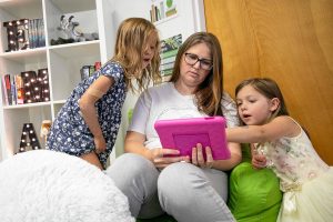 Morgan Stewart, board member and wife of teacher Andrew Stewart, checks out a PBS app with students Morgan and Austin Gardea, 6 and 4 respectively, during an open house at the Everett Montessori Academy on Saturday, July 8, 2023, in downtown Everett, Washington. (Ryan Berry / The Herald)