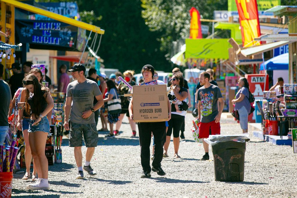 A Boom City patron walks between rows of stands with a box labeled HYDROGEN BOMB on July 1, 2023, in Tulalip, Washington. (Ryan Berry / The Herald)