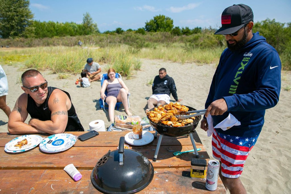 Samil Pillay, of Everett, grills a batch of chicken wings while spending a day at the Jetty Island beach with friends. (Ryan Berry / The Herald)