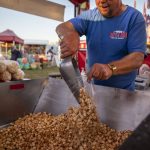 Unique Kettle Korn co-owner Jim Huff, 55, scoops popcorn into a bag during the Kla Ha Ya Days carnival at Harvey Field in Snohomish, Washington on Thursday, July 13, 2023. (Annie Barker / The Herald)