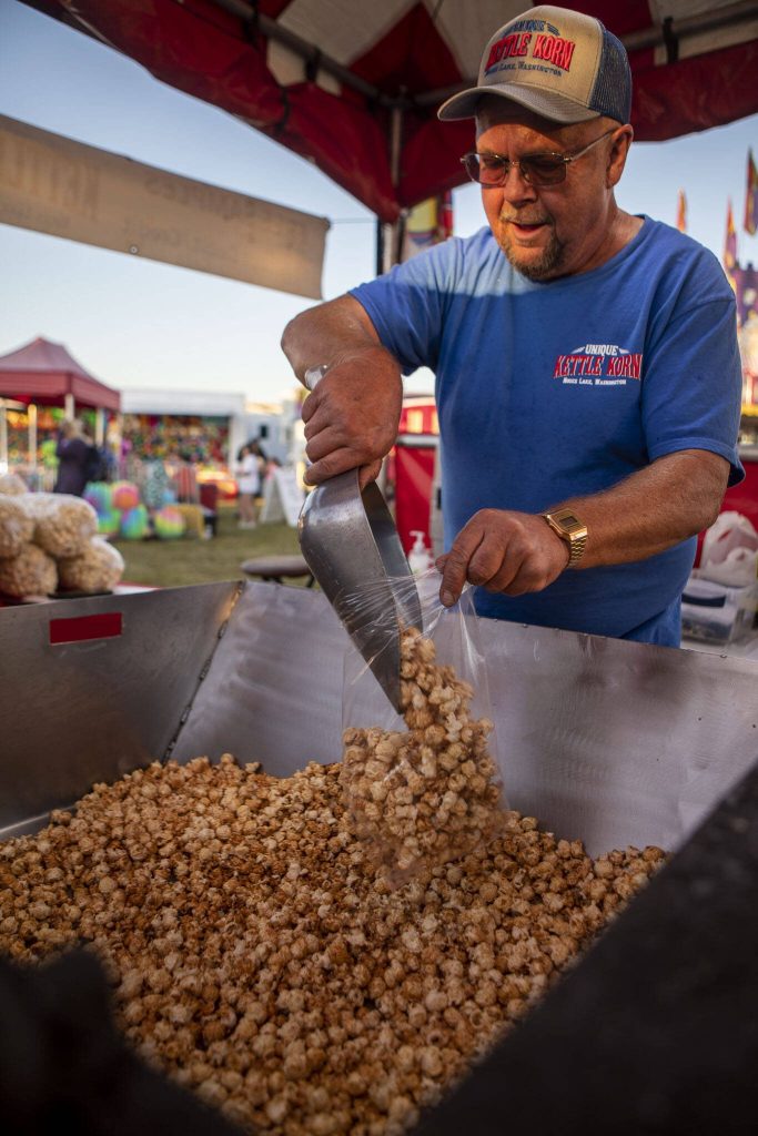 Unique Kettle Korn co-owner Jim Huff, 55, scoops popcorn into a bag during the Kla Ha Ya Days carnival at Harvey Field in Snohomish, Washington on Thursday, July 13, 2023. (Annie Barker / The Herald)