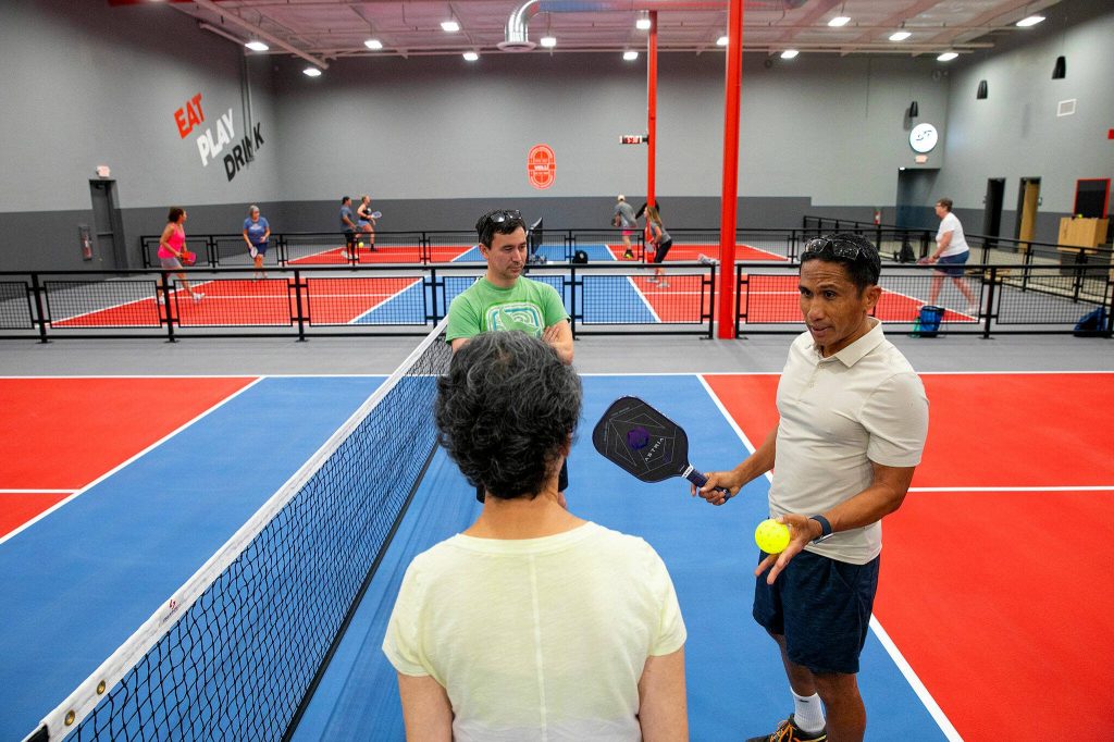 Nick Patterson and his mother, Mary Jane Patterson, receive some pickleball pointers from Ed Sarausad, right, on Wednesday at VOLLI in Marysville. (Ryan Berry / The Herald)