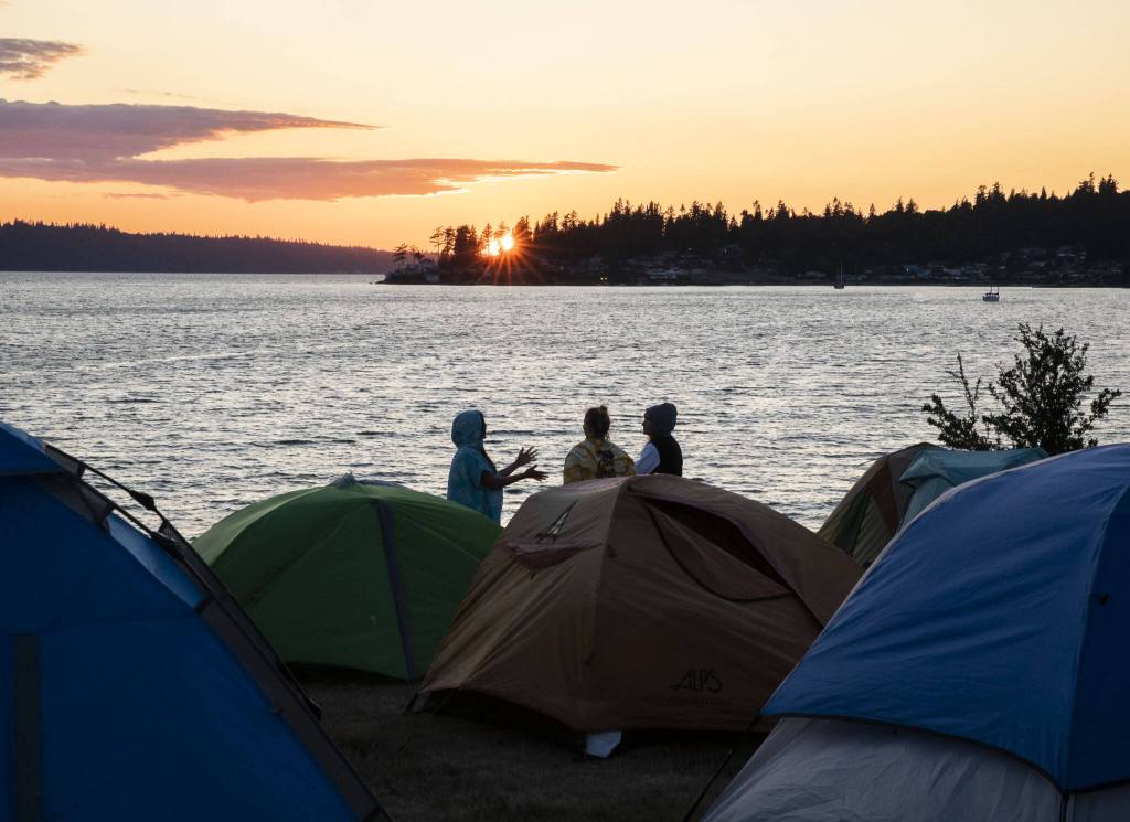 People chat outside of their tents sent up along the shoreline of Tulalip Bay as the sun sets on Thursday, July 27, 2023 in Tulalip, Washington. (Olivia Vanni / The Herald)