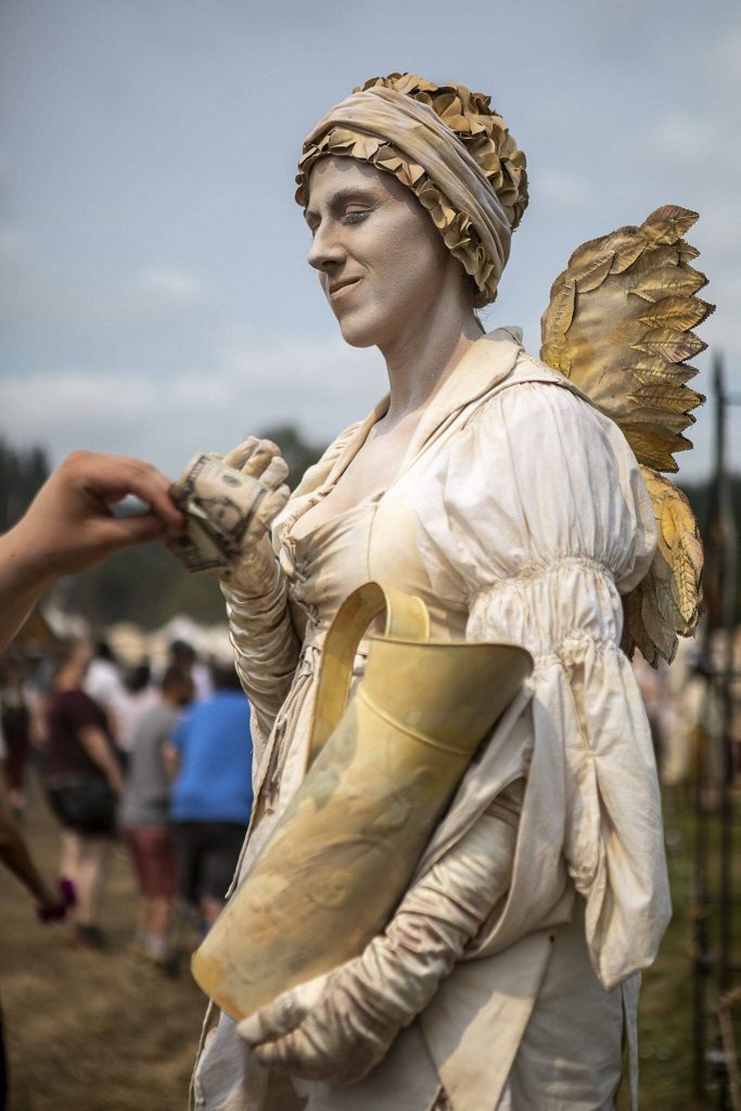 Faye, the living statue, accepts tips in their pitcher during the Washington Midsummer Renaissance Faire at Sky Meadows Park in Snohomish, Washington, on Sunday, Aug. 6, 2023. (Annie Barker / The Herald)