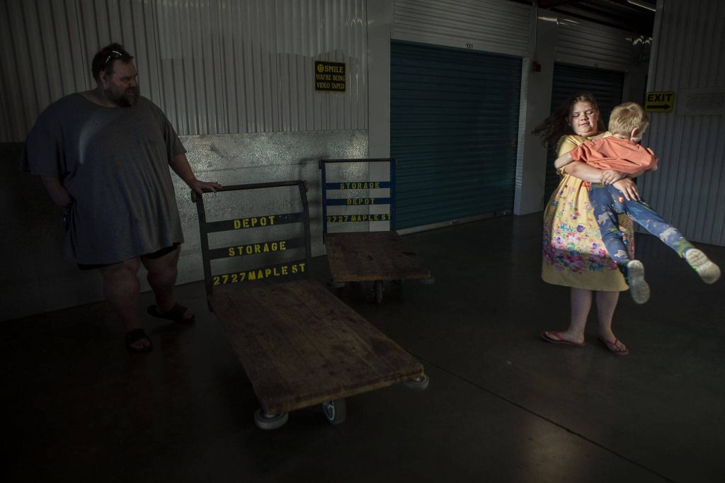 Marc Boucher, left, watches as Makayla Boucher, 11, spins her brother Maverick, 4, at the Everett Self Storage Depot, at 2727 Maple St. in Everett, Washington, on Wednesday, Aug. 2, 2023. (Annie Barker / The Herald)