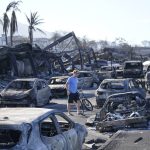 A man walks through wildfire wreckage Friday, Aug. 11, 2023, in Lahaina, Hawaii.  Hawaii emergency management records show no indication that warning sirens sounded before people ran for their lives from wildfires on Maui that wiped out a historic town.  (AP Photo/Rick Bowmer)