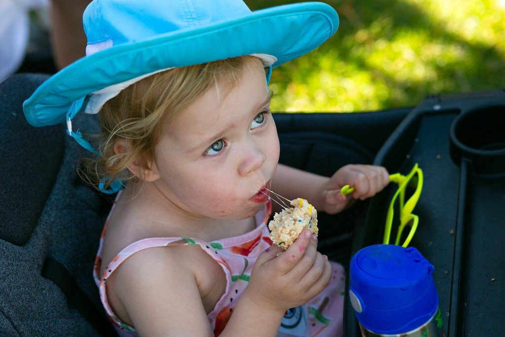 Remi Thornton, 3, enjoys a birthday cake Marshmallow Crispy bar from Browned & Toasted in the shade during Taste Edmonds on Saturday, August 12, 2023, at Frances Anderson Play Field in Edmonds, Washington. (Ryan Berry / The Herald)