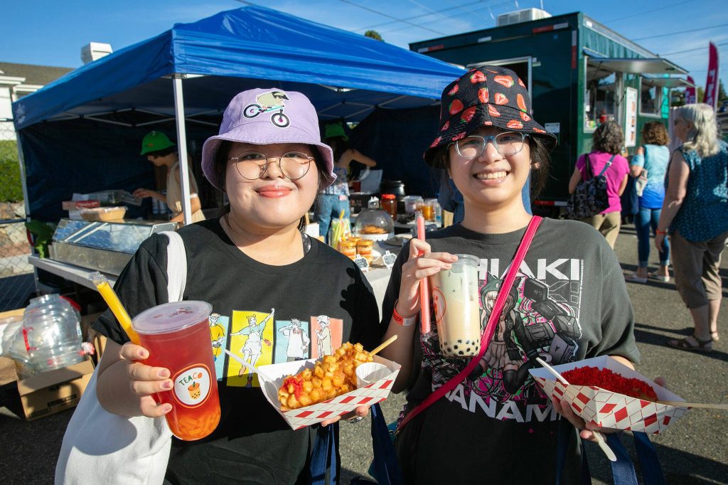 Angelina Kha, left, and Davina Nguyen show off their choices from TeaCo Tea House and Seoul Hotdog during Taste Edmonds on Saturday, August 12, 2023, at Frances Anderson Play Field in Edmonds, Washington. (Ryan Berry / The Herald)
