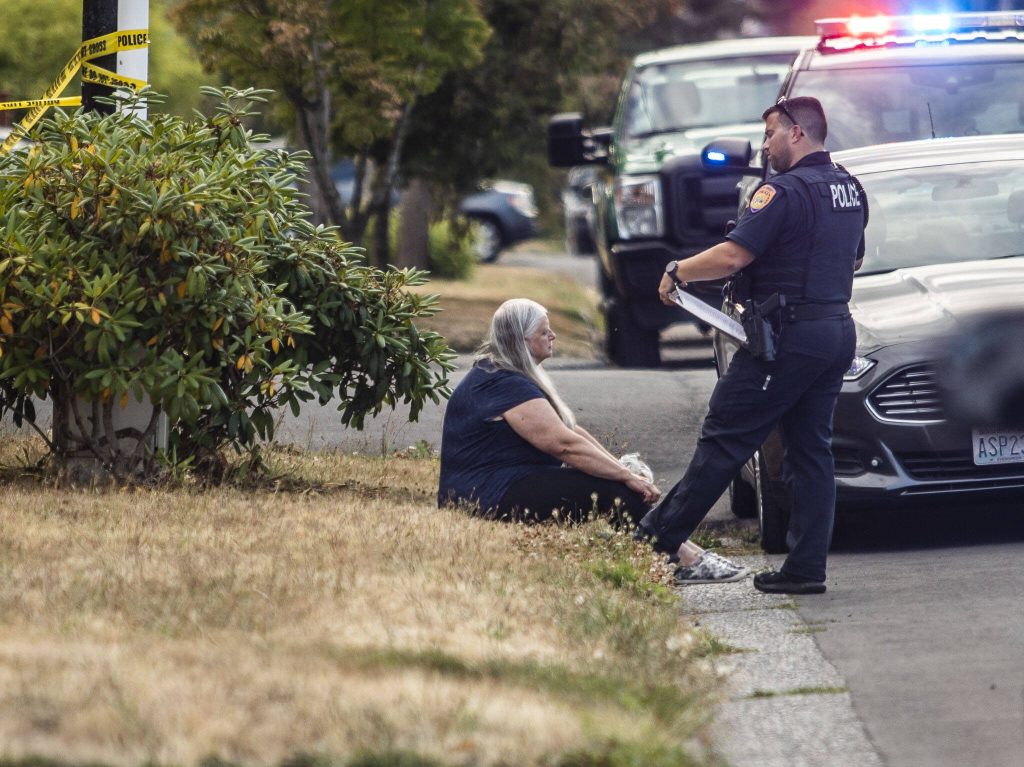 Everett police speak with a woman seated on a curb along 23rd Street on Tuesday, Aug. 22, 2023 in Everett, Washington. (Olivia Vanni / The Herald)