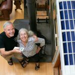Homeowners Jim and Chris Hall stand beneath their new heat pump, at right, inside their Whidbey Island home on Thursday, Sep. 7, 2023, near Langley, Washington. The couple, who are from Alaska, have decreased their use of their wood burning stove to reduce their carbon footprint. (Ryan Berry / The Herald)