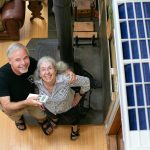 Homeowners Jim and Chris Hall stand beneath their new heat pump, at right, inside their Whidbey Island home on Thursday, Sep. 7, 2023, near Langley, Washington. The couple, who are from Alaska, have decreased their use of their wood burning stove to reduce their carbon footprint. (Ryan Berry / The Herald)