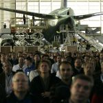 As workers put the finishing touches on a Boeing 777 airplane in the background, Wednesday, Dec. 6, 2006 in Everett, Washington, hundreds of employees view a computer simulation of what the official roll-out of the new 787 airplane might look like when it is unveiled in 2007 as part of a virtual rollout demonstration. (AP Photo/Ted S. Warren)