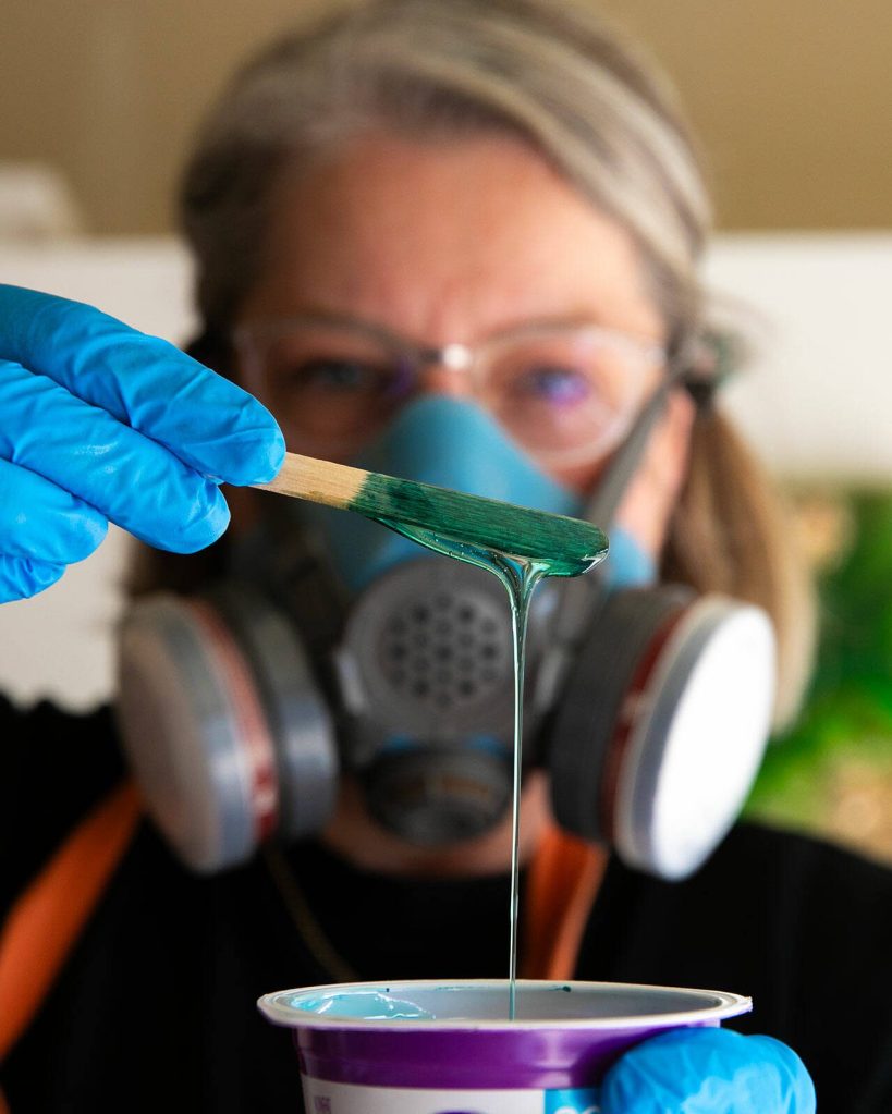 Downes checks the color of her resin as she adds dye before applying the material to a canvas. (Ryan Berry / The Herald)