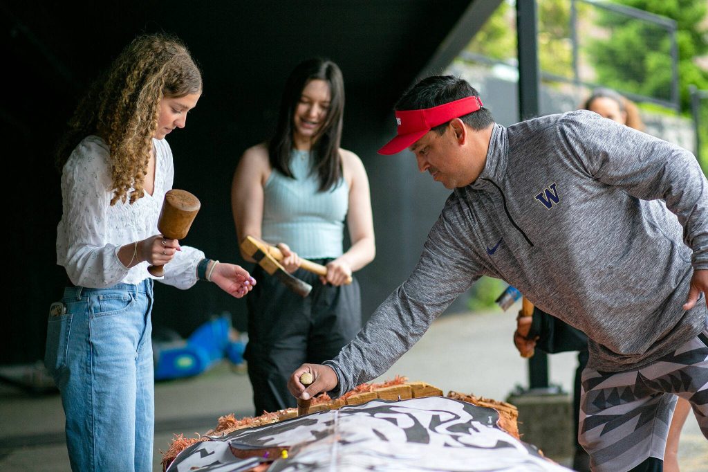 James Madison shows Archbishop Murphy students Lauren Fogliani (left) and Frankie Wanamaker how to use their tools as they help carve away pieces of wood. (Ryan Berry / The Herald)