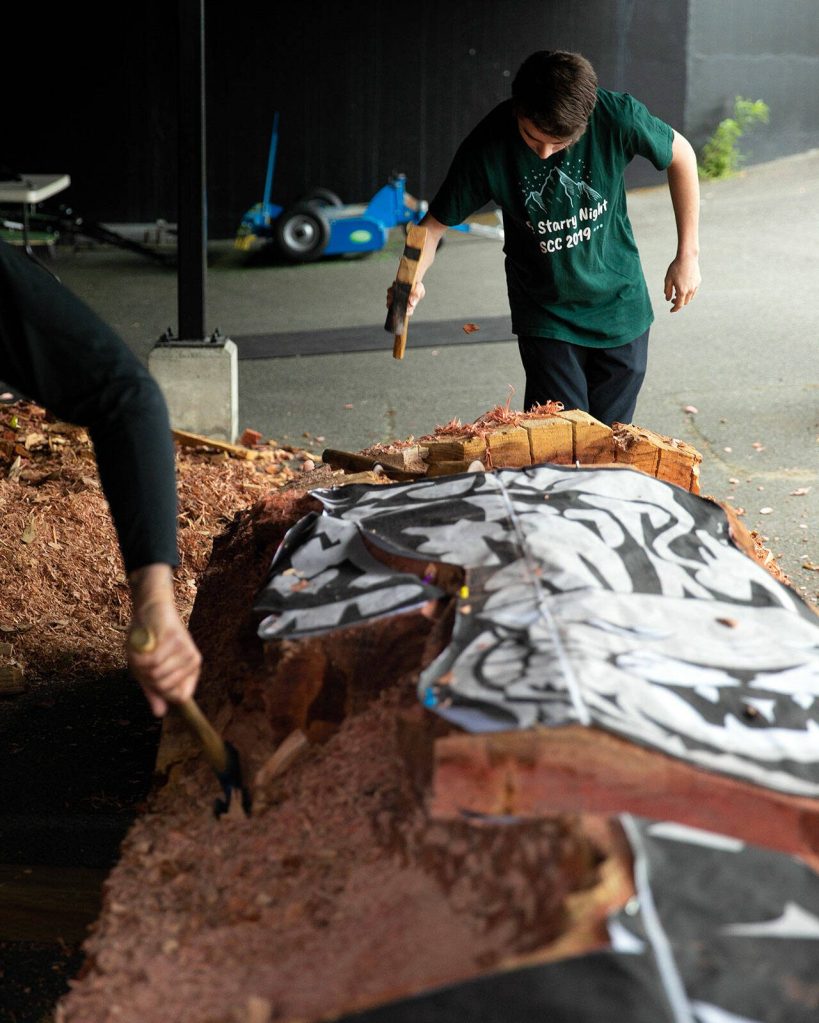 Junior Cory Maxwell takes a turn using an adze to chip away at a healing pol. (Ryan Berry / The Herald)