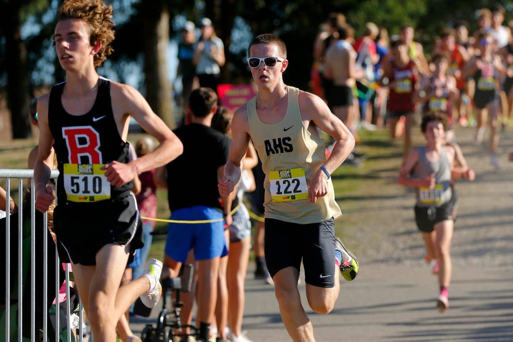 An Arlington runner keeps pace with a runner from Bozeman, Mont. during the Hole in the Wall Cross Country Invitational on Saturday, Oct. 7, 2023, at Lakewood High School in Arlington, Washington. (Ryan Berry / The Herald)