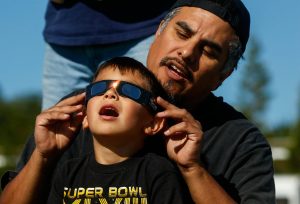 Just off Paine Field near the Future of Flight Aviation Center, Ben Flores of Mukilteo helps his son Vincent view the solar eclipse through certified safety glasses on August 21, 2017. (Dan Bates / The Herald file)