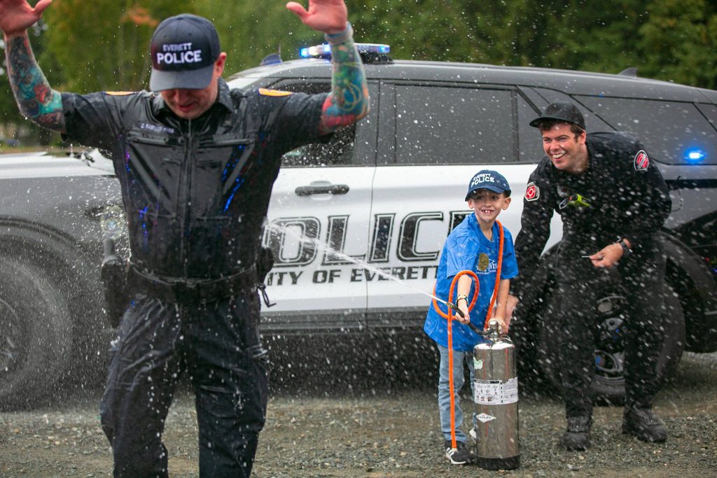 Make-A-Wish kid Carson, 7, hoses down Everett Police Recruiting Officer Danny Rabelos during a surprise Make-A-Wish sendoff Saturday, Oct. 21, 2023, at Thornton A. Sullivan Park in Everett, Washington. (Ryan Berry / The Herald)