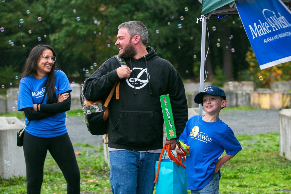 Carson and his dad Tyler Ackley smile as they take in the moment at a surprise Make-A-Wish sendoff Saturday, Oct. 21, 2023, at Thornton A. Sullivan Park in Everett, Washington. (Ryan Berry / The Herald)