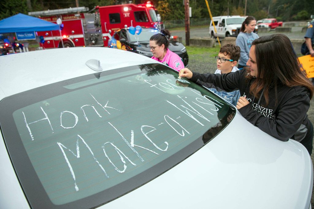 Brianna Haimes, right, and Robin Snyder of the Silvertips Booster Club, write on the family car at a surprise Make-A-Wish sendoff for Carson on Saturday, Oct. 21, 2023, at Thornton A. Sullivan Park in Everett, Washington. (Ryan Berry / The Herald)