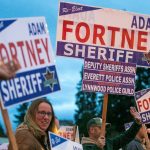 Snohomish County Sheriff Adam Fortney waves signs with supporters along Highway 9 on Monday, Nov. 6, 2023, in Arlington, Washington. (Ryan Berry / The Herald)