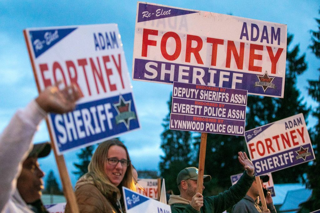 Snohomish County Sheriff Adam Fortney waves signs with supporters along Highway 9 on Monday, Nov. 6, 2023, in Arlington, Washington. (Ryan Berry / The Herald)