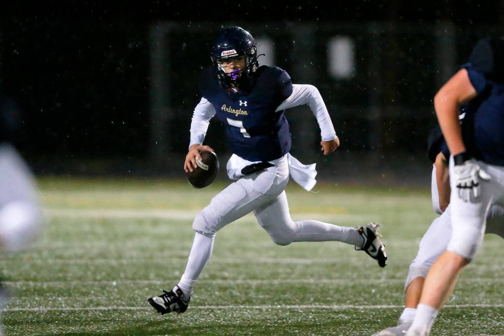 Arlington junior quarterback Leyton Martin rolls out of the pocket against Ridgeline during a playoff matchup Friday, Nov. 10, 2023, at Arlington High School in Arlington, Washington. (Ryan Berry / The Herald)