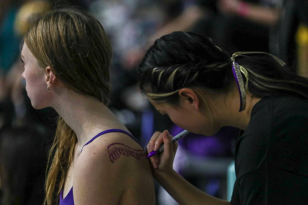 A swimmer draws wings on a fellow swimmer during the 4A girls state swim and dive championships at King County Aquatic Center in Federal Way, Washington on Saturday, Nov. 11, 2023. (Annie Barker / The Herald)