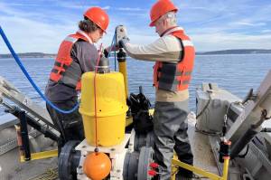 Sam Tabbutt and Jason Wood from SMRU Consulting connect an acoustic release to the hydrophone, so the boat can lower the device to the seabed and then disconnect from it. (Rachel Aronson)