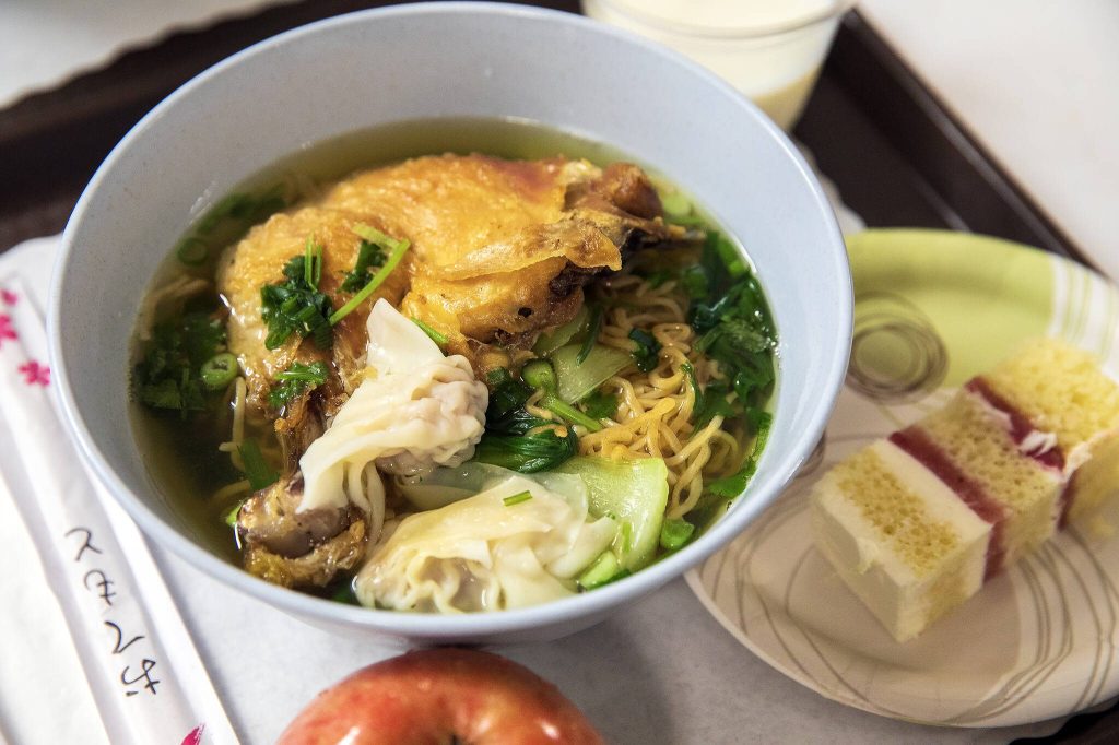 Fried chicken noodle soup is served with an apple and cake.