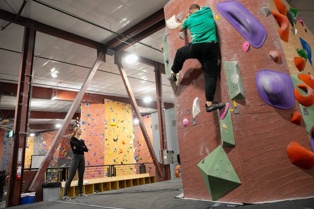 Aja Van Hout, left, takes a breather and watches other climbers boulder at Vertical World North on Monday, Nov. 20, 2023, in Lynnwood, Washington. (Ryan Berry / The Herald)