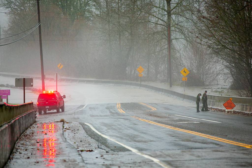 A group of park rangers have a look at the flood waters along the Stillaguamish on Highway 530 after closing down Twin Rivers Park during heavy flooding on Tuesday, Dec. 5, 2023, in Arlington, Washington. (Ryan Berry / The Herald)