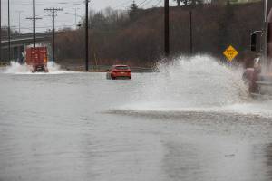 Semi trucks drive around a flooded car along Marine View Drive on Tuesday, Dec. 27, 2022 in Everett, Washington. (Olivia Vanni / The Herald)