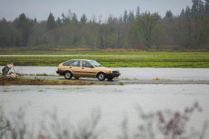 A vehicle turns onto 212th Street NE and crosses over a small amount of water on Thursday, Dec. 7, 2023, after extensive flooding from the Stillaguamish River in Silvana, Washington. (Ryan Berry / The Herald)
