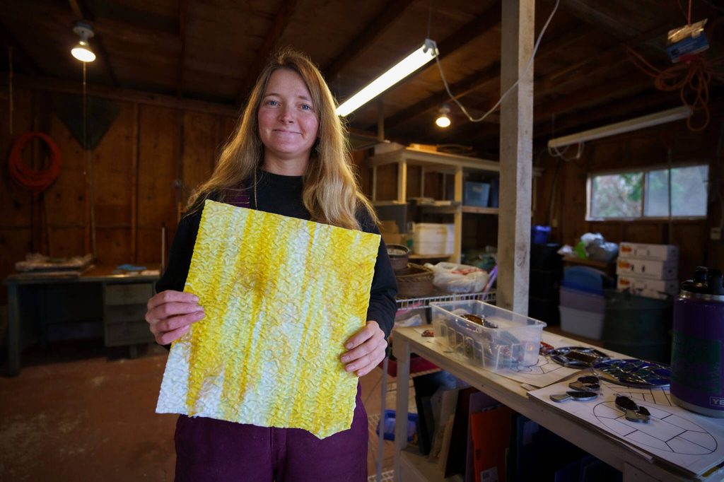 Mackensie Bennett holds up a sheet of yellow glass with a wavy texture. (Photo by David Welton)