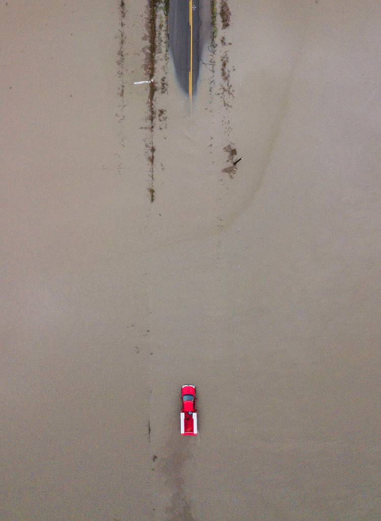 A red truck navigates through floodwaters covering 28th Avenue NW along Pioneer Highway on Wednesday, Dec. 6, 2023, in Stanwood, Washington. Communities near the mouth of the Stillaguamish River remained flooded that day in the aftermath of a major rainstorm. Emergency crews responded to at least 13 rescues. (Olivia Vanni / The Herald)