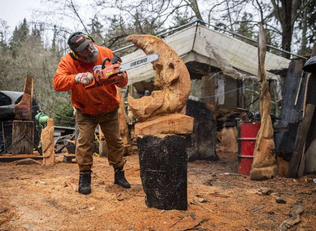 Steve Backus works on the details of a moon carving at his woodshop and home on Whidbey Island on Monday, Feb. 6, 2023. Steve Backus, a generational woodcarver, lost a portion of his shop to a fire. In the fire, he lost a large catalog of work, in addition to tools and other woodworking items he had accumulated over the years. (Olivia Vanni / The Herald)