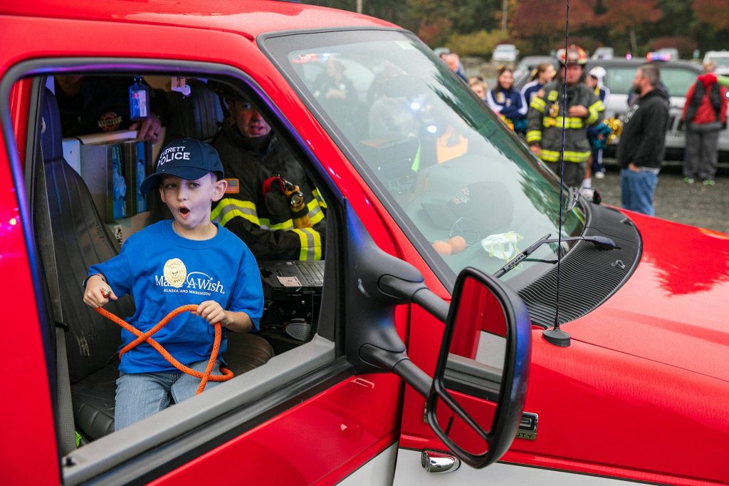 Carson, 7, reacts with shock as he gets an opportunity to use some of the gear inside an Everett ambulance during a surprise Make-a-Wish sendoff Saturday, Oct. 21, 2023, at Thornton A. Sullivan Park in Everett, Washington. Dozens of first responders, family and community members rallied together to lift up Carson before he and his family headed off to Disneyland. (Ryan Berry / The Herald)